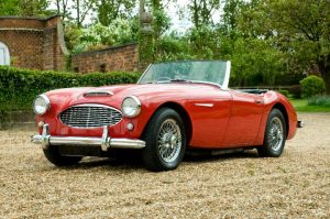 Stunning red classic Austin-Healey convertible parked on a gravel driveway in East Peckham. Beautiful vintage sports car with wire wheels, perfect for car enthusiasts.