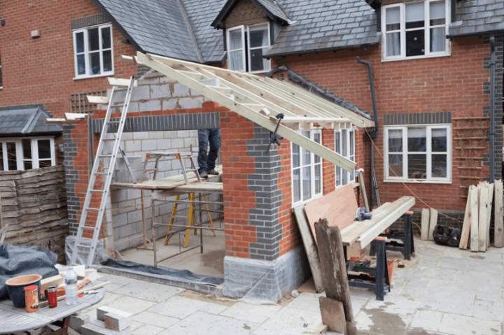 Progress shot of a residential home extension being built in East Peckham. Features brickwork, timber framing, scaffolding, and building materials on a paved patio.

