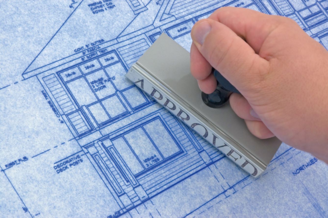 a hand stamping an approved message on building plans